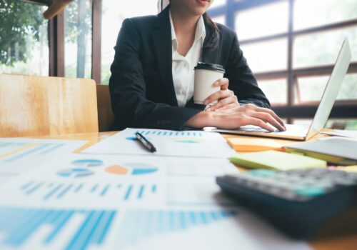 Woman drinking coffee working on a computer in front of business documents