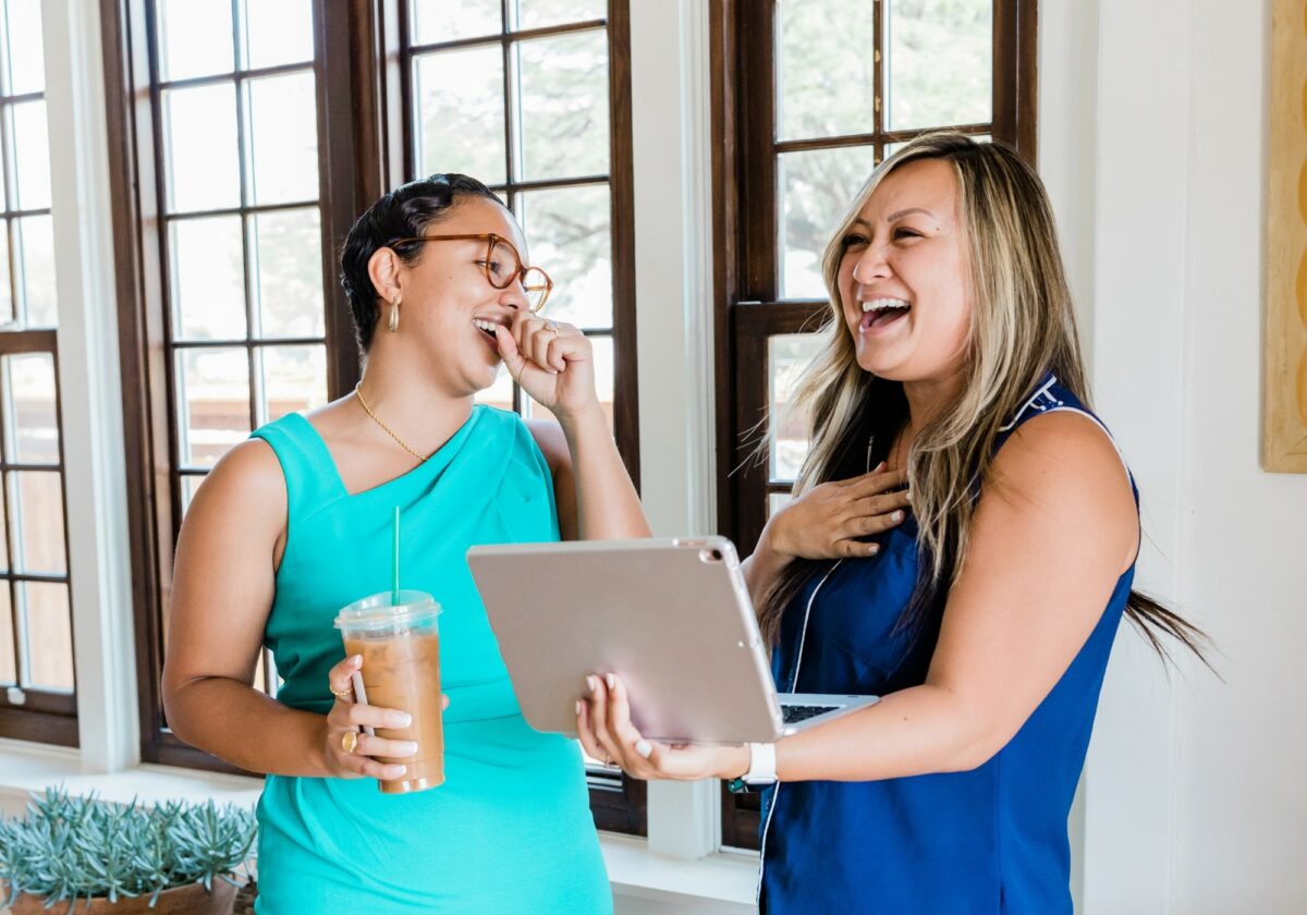 Two women laughing while talking holding a tablet