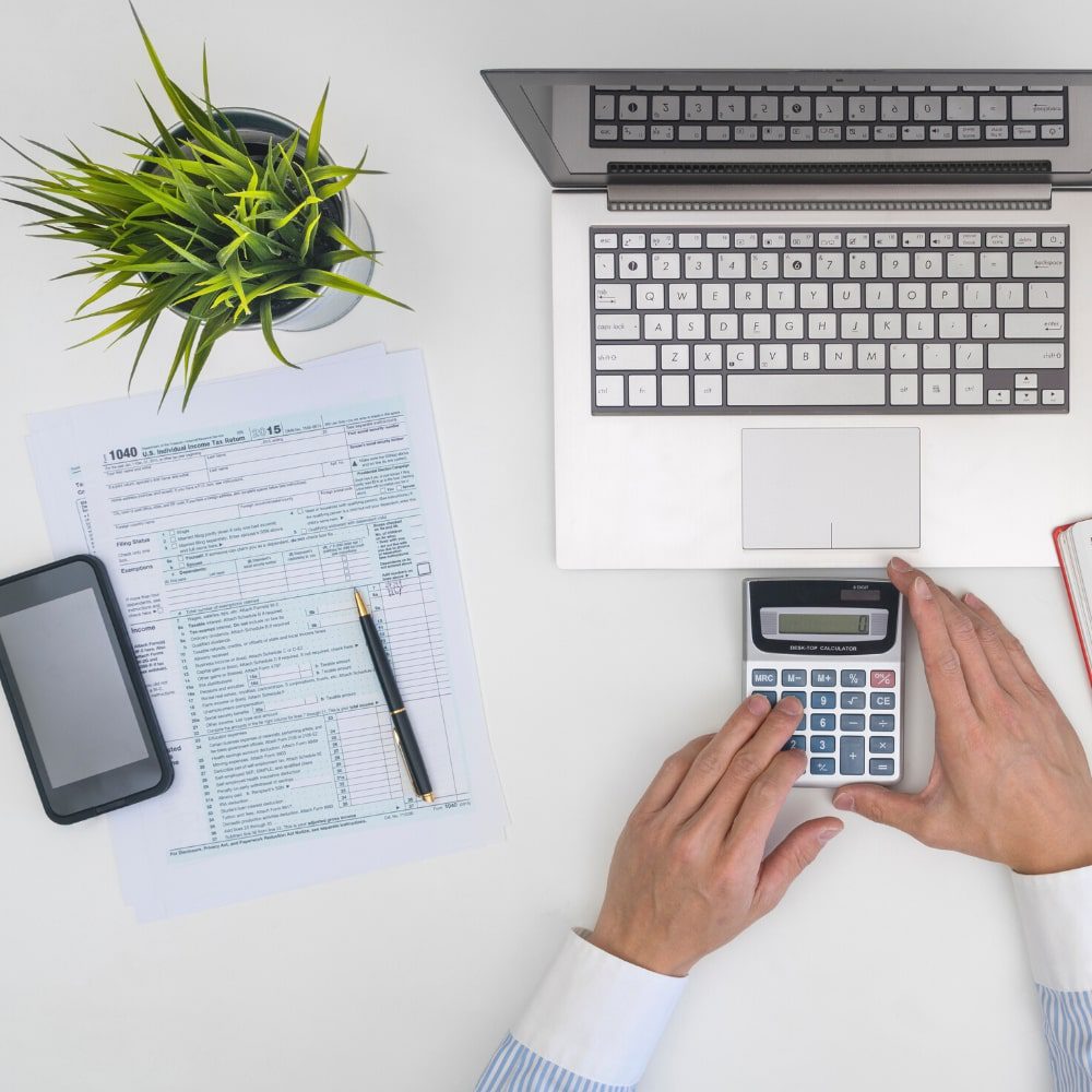 Tax forms laptop and calculator on a desk